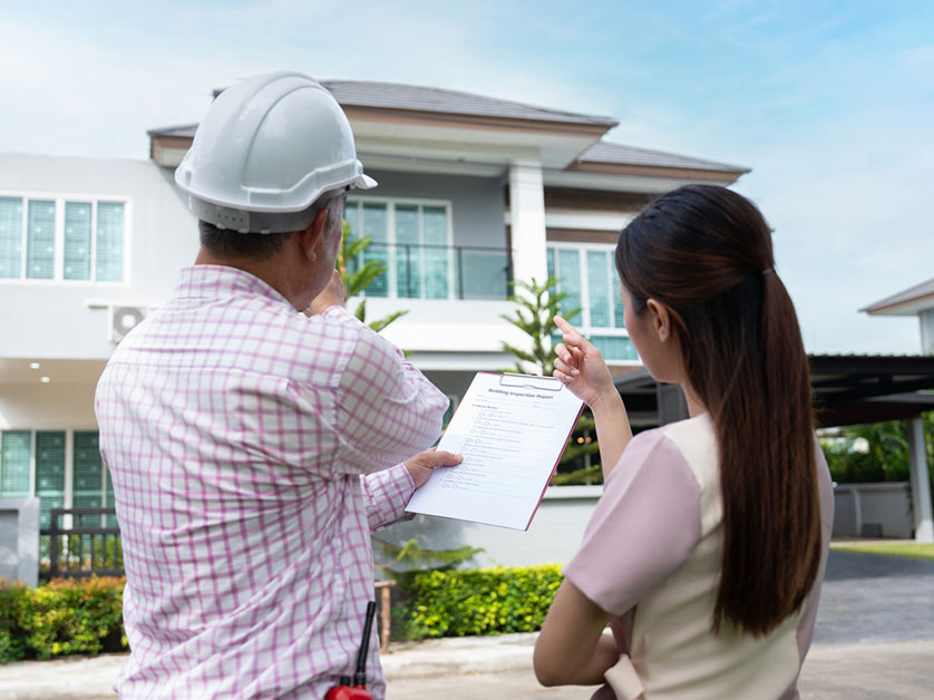 An inspector and a homeowner or buyer examining a building inspection report at a property.