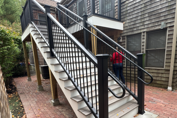 Exterior staircase with white steps and black railings leading to a deck on a cedar-shingled building.