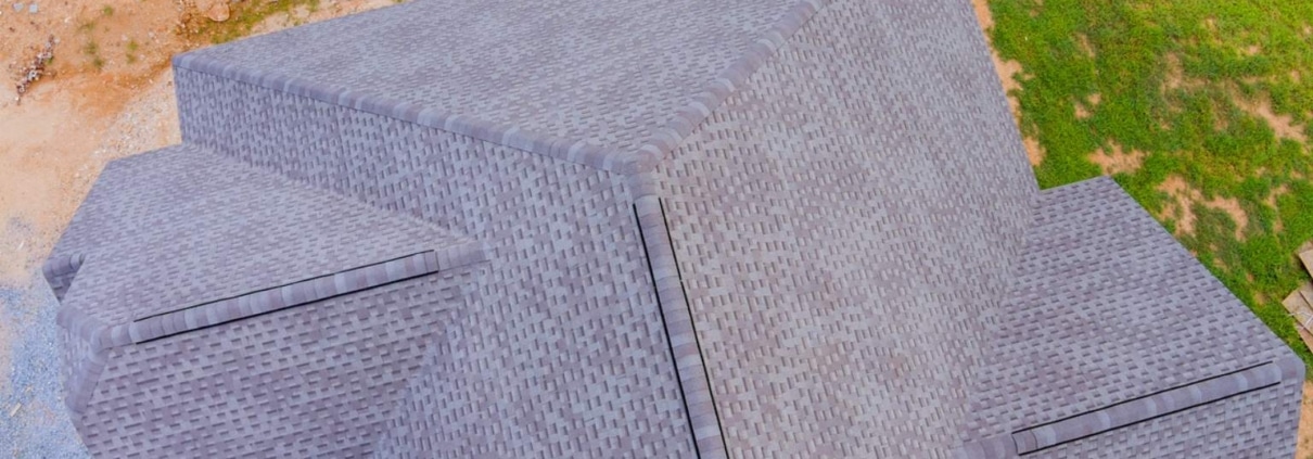 aerial shot of a finished gray shingle roof with clean ridge lines, next to construction dirt and lawn.
