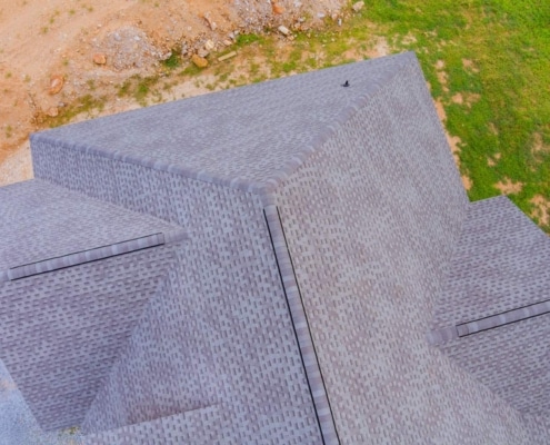 aerial shot of a finished gray shingle roof with clean ridge lines, next to construction dirt and lawn.