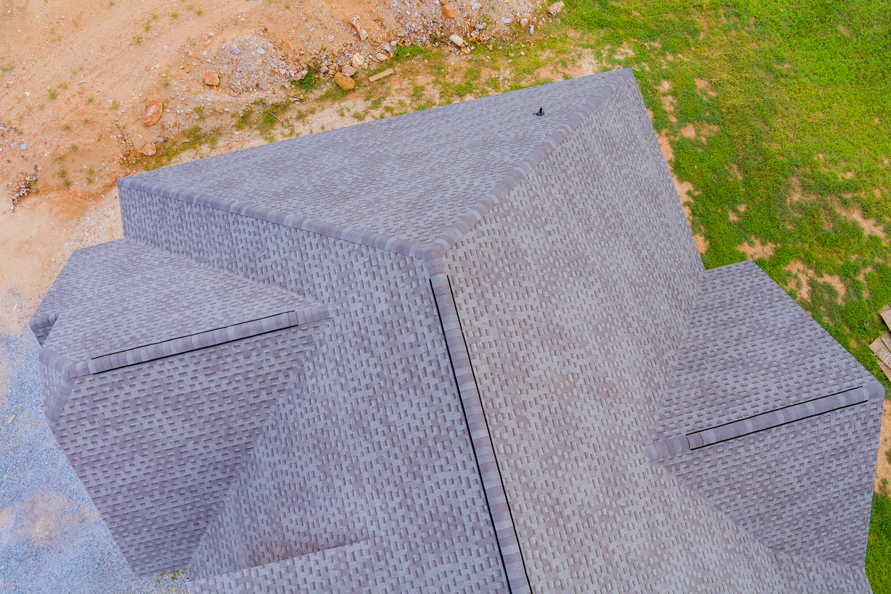 aerial shot of a finished gray shingle roof with clean ridge lines, next to construction dirt and lawn.