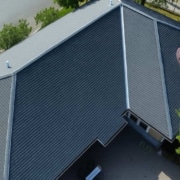 Precision in Action1 Aerial view of a large roof installation featuring dark gray standing seam metal panels and two distinctive semicircular copper-toned dormer vents.