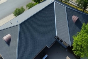 Aerial view of a large roof installation featuring dark gray standing seam metal panels and two distinctive semicircular copper-toned dormer vents.