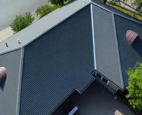 Aerial view of a large roof installation featuring dark gray standing seam metal panels and two distinctive semicircular copper-toned dormer vents.