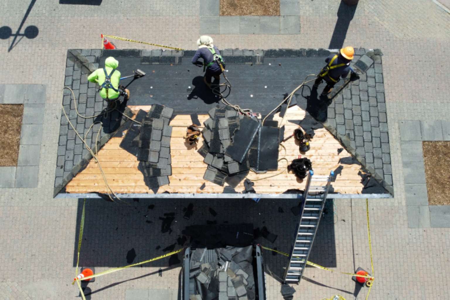 Drone shot of roofers working on a flat roof, wearing high-visibility vests and surrounded by supplies.