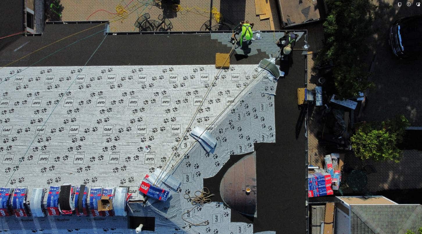 Drone shot of roofers working on a flat roof, wearing high-visibility vests and surrounded by supplies.
