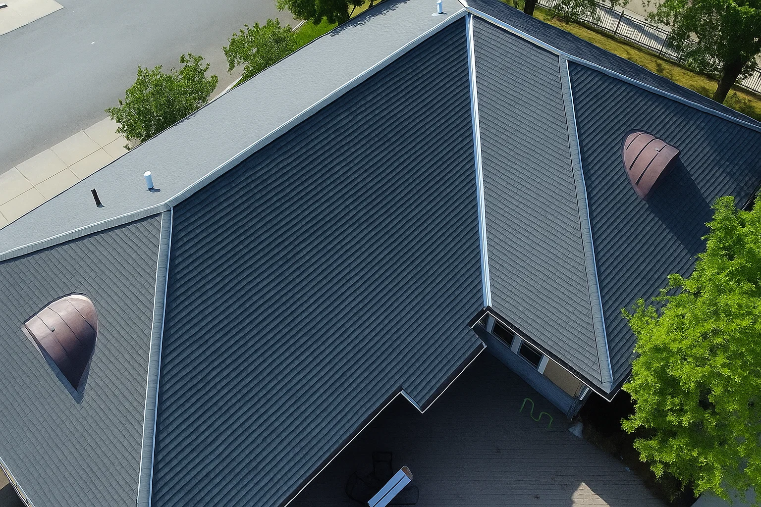 Aerial view of a large roof installation featuring dark gray standing seam metal panels and two distinctive semicircular copper-toned dormer vents.