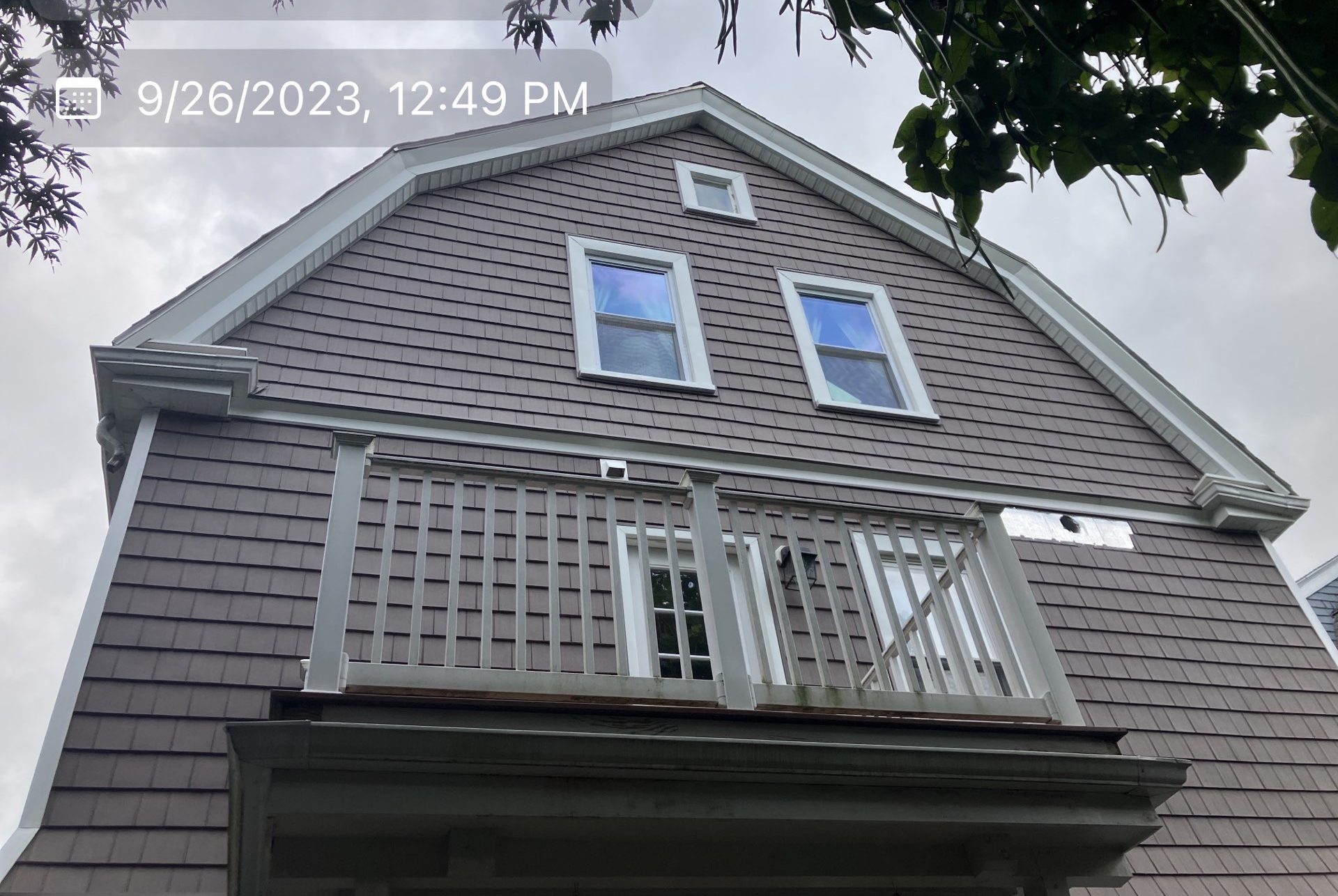2023-09-26 16 49 03Z-ln0jy3ccghyn32or Gable end of a house with new brown shingle-style siding, white trim, and a second-story balcony with a white railing.