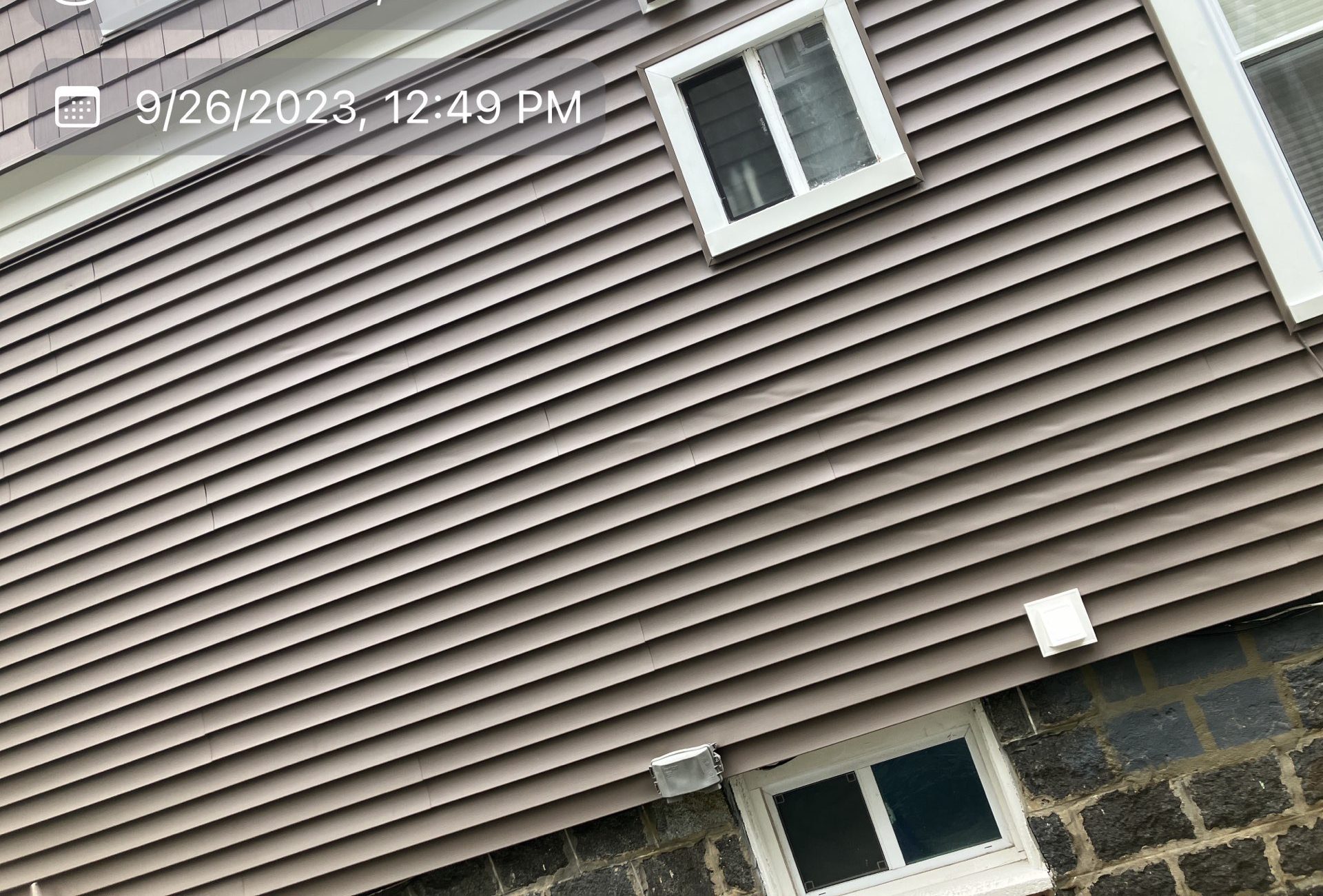 2023-09-26 16 49 59Z-ln0jzajsjbupejq5 new brown horizontal siding on a house, featuring two small windows with white trim and a dark, stone foundation at the bottom.