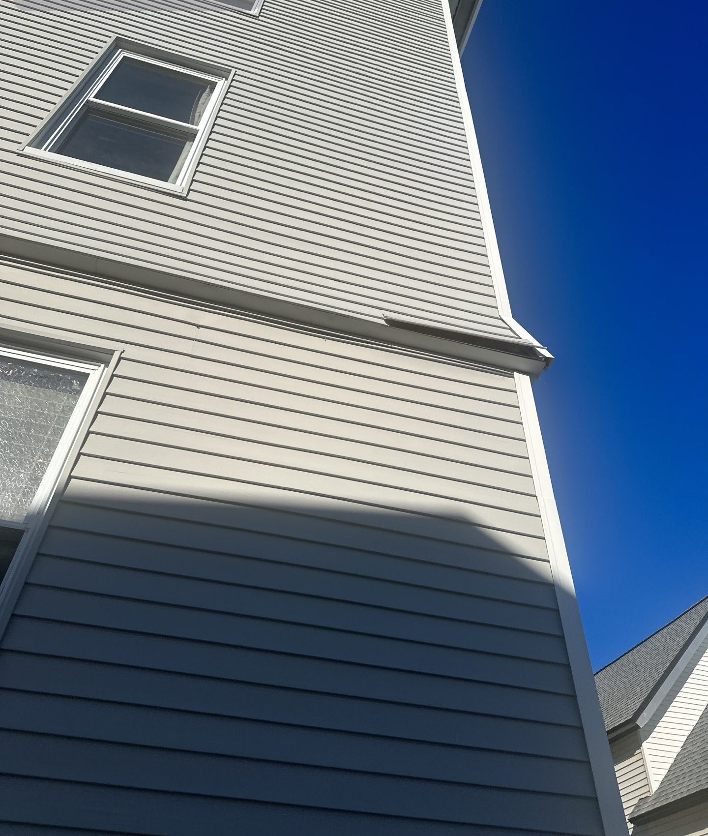 2024-01-05 17 56 47Z-lr0xu8wf2drvegv0 light gray horizontal siding and a window corner against a bright blue sky.
