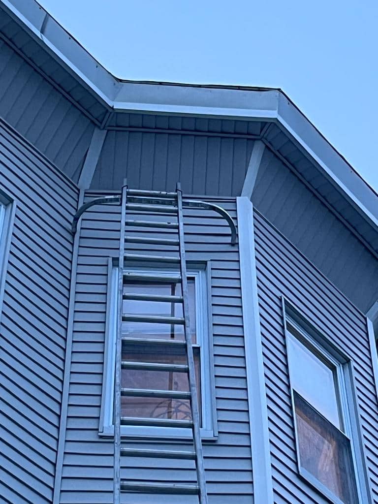2024-01-19 16 33 32Z-lrkv13oa5lguukf5 Fire escape ladder mounted over a window on a blue-gray sided building.