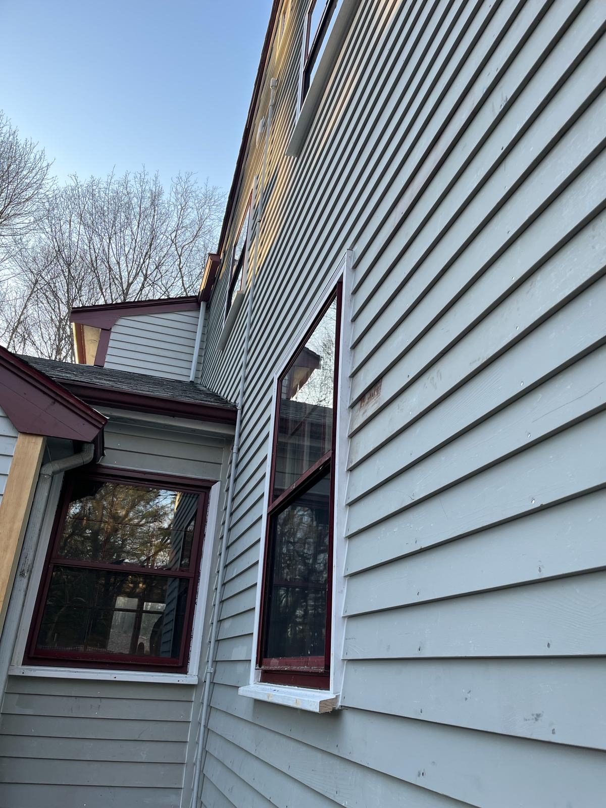 2024-02-26 21 59 50Z-lt3hf3f7czkp69u2 Corner of a light gray house with new vertical wood trim, dark shutters, and red-trimmed windows.