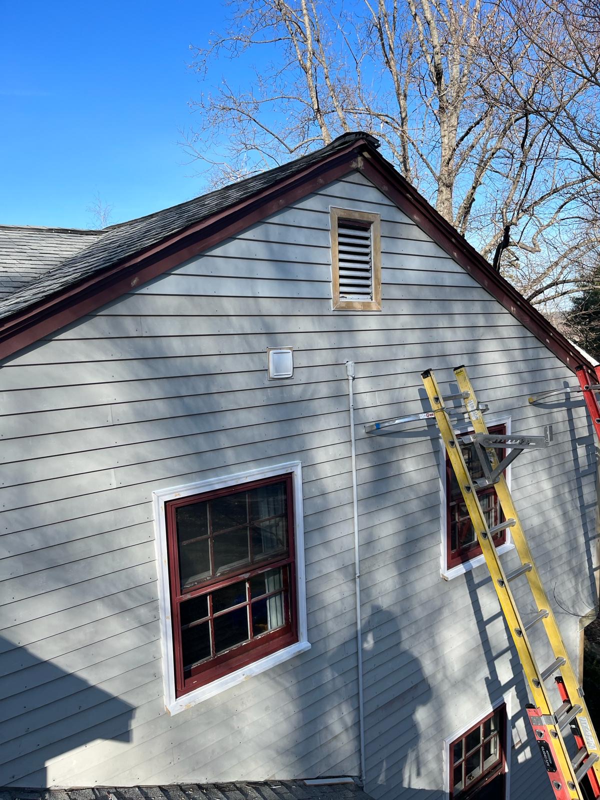 2024-02-26 21 59 50Z-lt3hf3fuipzfld5p Side of a light gray house undergoing trim replacement next to a garage, with a bare tree in the foreground.