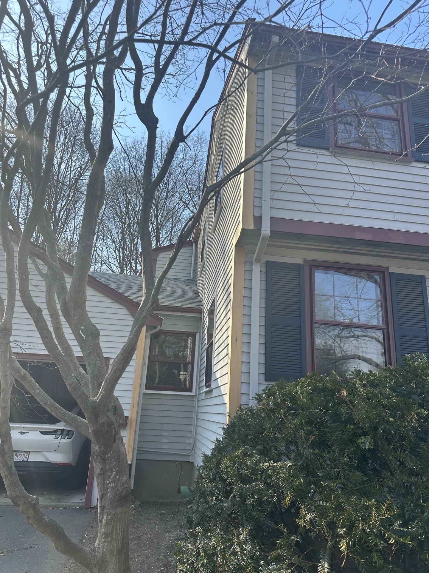 2024-02-27 21 07 17Z-lt4uzdsz5ugv1b4j Exterior corner of a two-story house with light siding and exposed wood trim, viewed through bare tree branches.