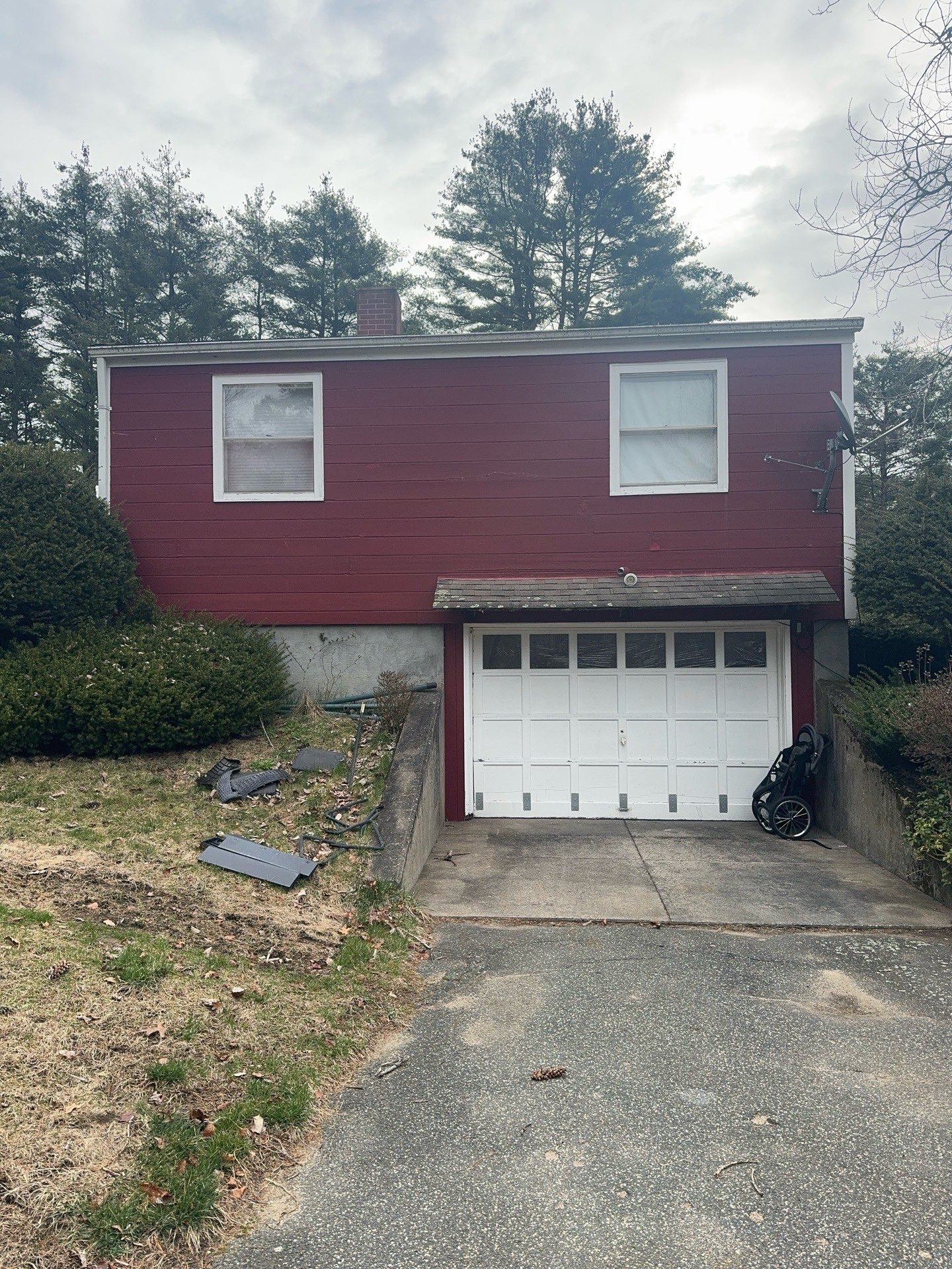 2024-04-02 13 28 12Z-luiezt2oq99gdpvl Red house with a white garage door and large trees in the background under a gray sky.