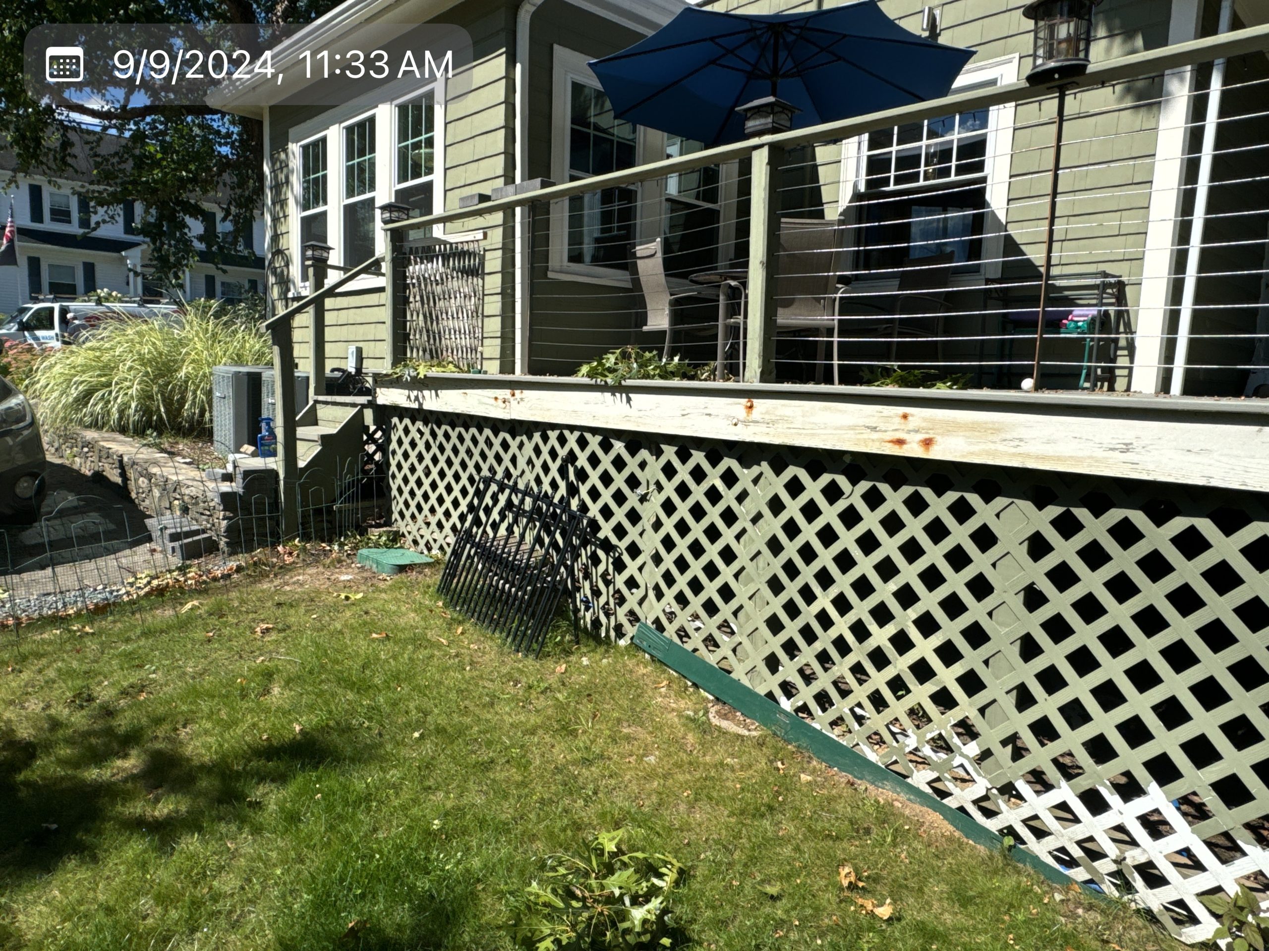 2024-09-09 15 33 39Z-m0v5xfkrcrry5jyf View of a house deck's corner and lattice foundation skirting next to a lawn.