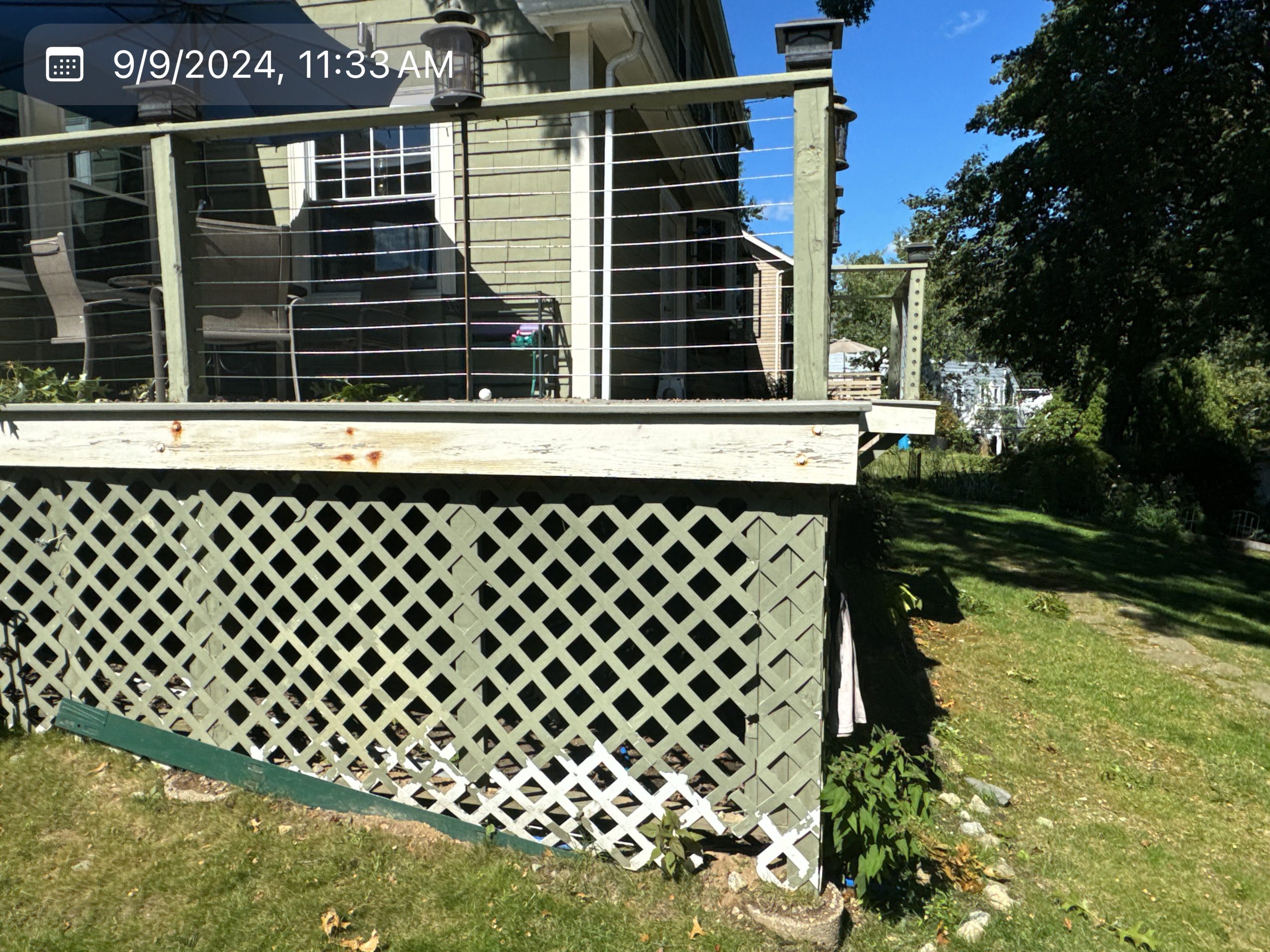 2024-09-09 15 33 40Z-m0v5xgev9szjywqq View of a house deck's corner and lattice foundation skirting next to a lawn.
