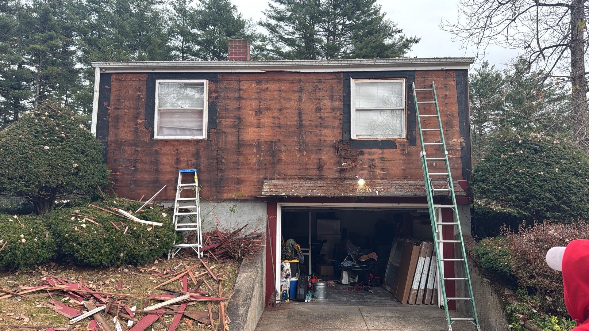 2024-11-04 16 00 19Z-m337jforjdbu5scl House exterior with siding removed, revealing dark red sheathing, two upper windows, an open lower garage, and ladders for construction.