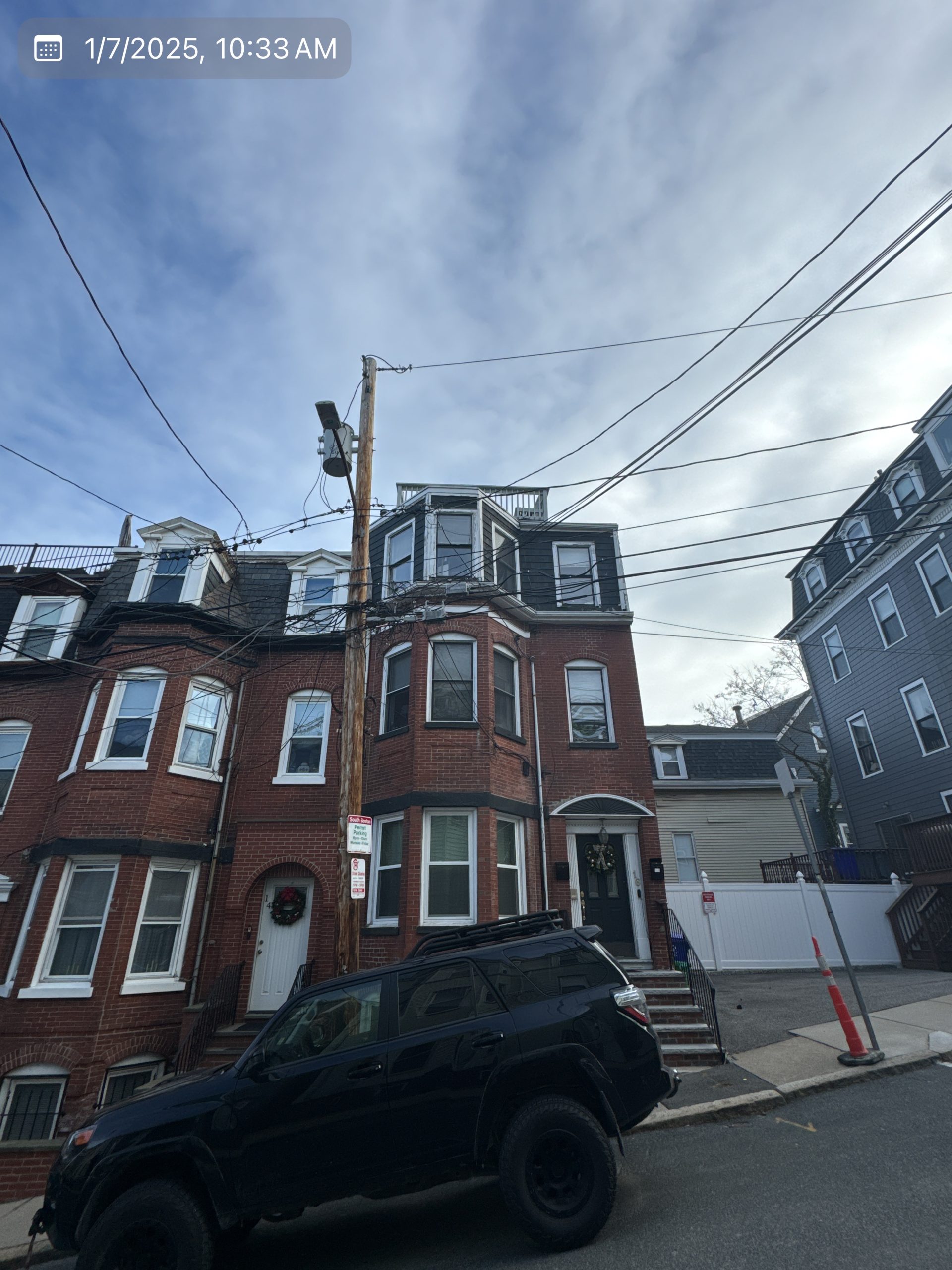 2025-01-07 15 33 52Z-m5mmrxorz5alyoxt Street view of a three-story brick apartment building with bay windows and a mansard roof on an overcast day.