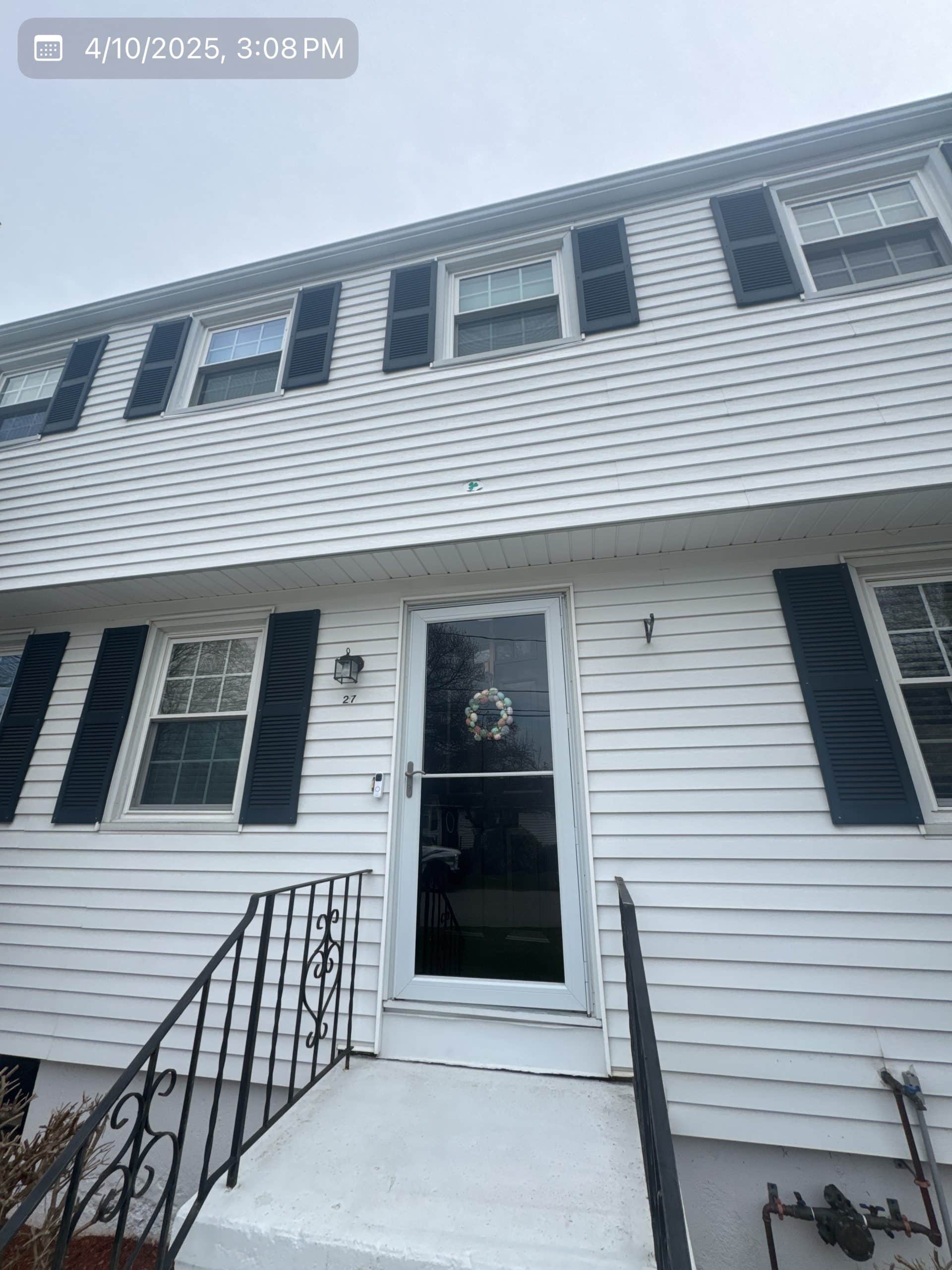 2025-04-10 19 08 26Z-m9bqe3b41gc484tl Front entrance of a two-story residence with white vinyl siding, black shutters, a glass storm door, and a black metal railing leading to the steps.