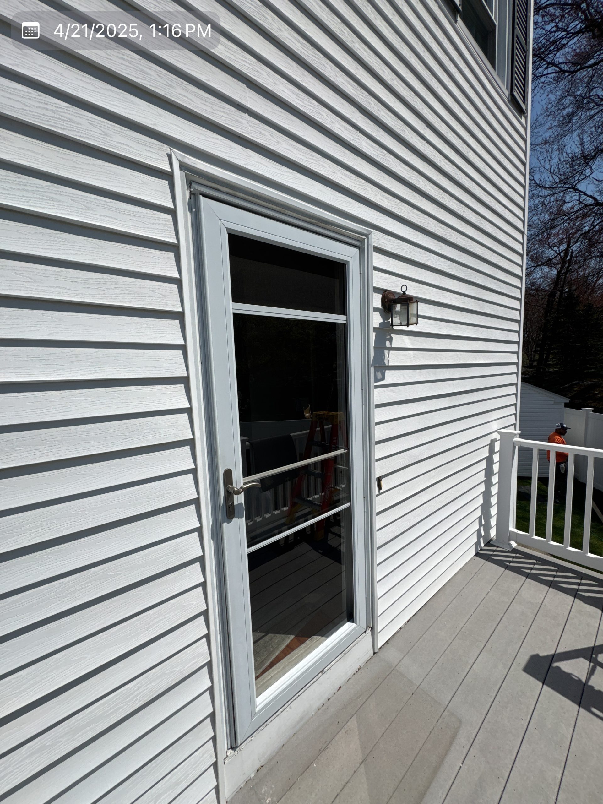 2025-04-21 17 16 31Z-m9rc8j26uat5p6no White glass storm door on a house with white horizontal siding, opening onto a gray deck with a white railing.