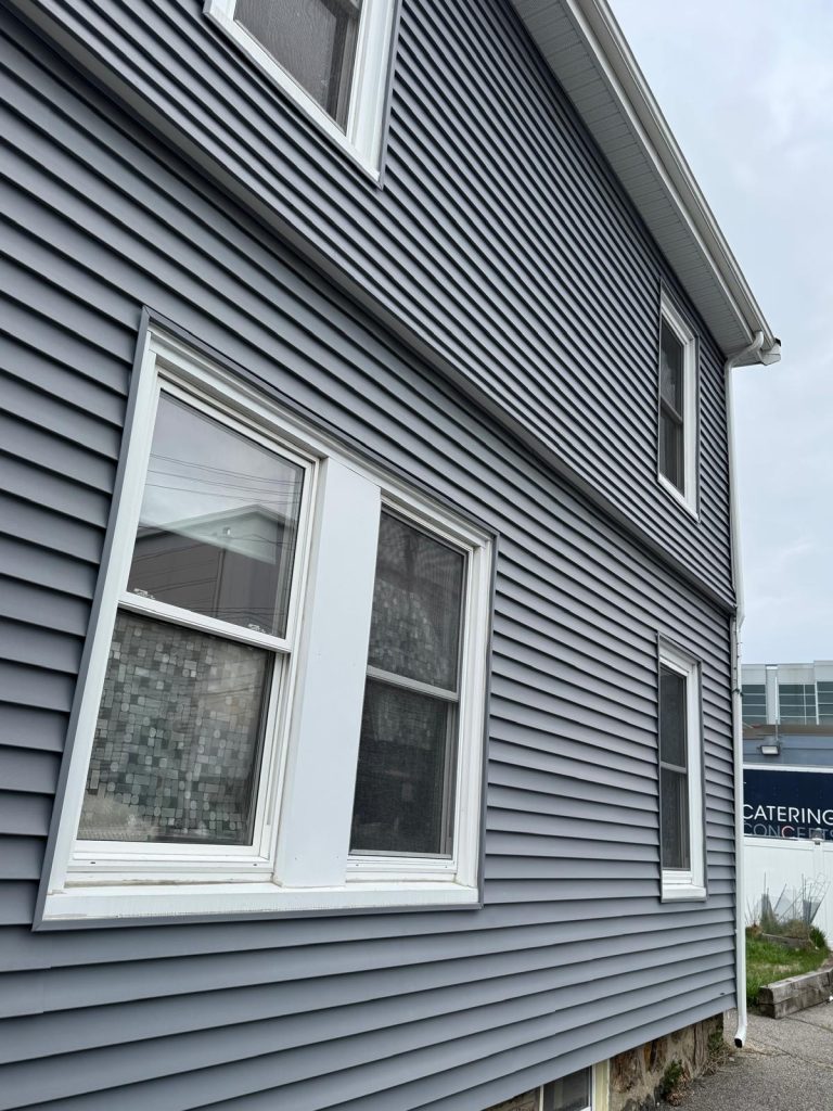 Exterior side of a building with new, dark gray horizontal siding and several white-trimmed windows, under an overcast sky.