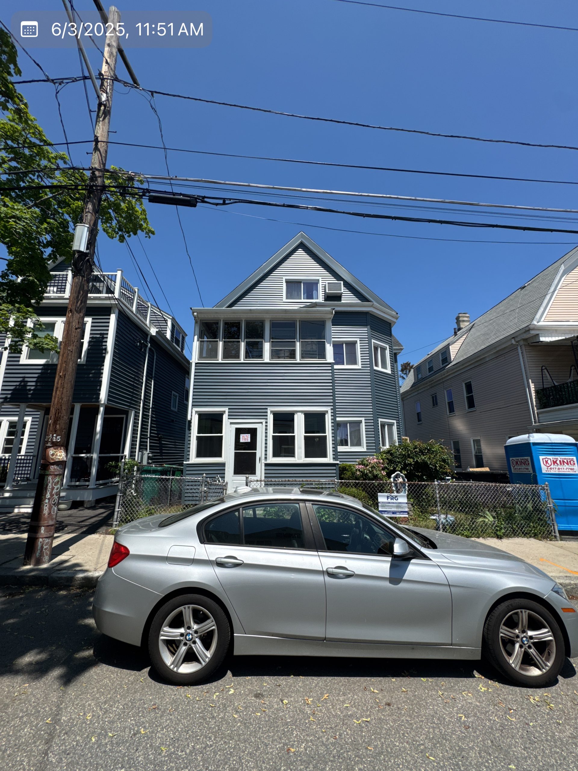 2025-06-03 15 51 52Z-mbgp5b6nhz6t0bxm Street view of a dark blue house with white trim, located between two other houses, with a silver sedan parked in the foreground.