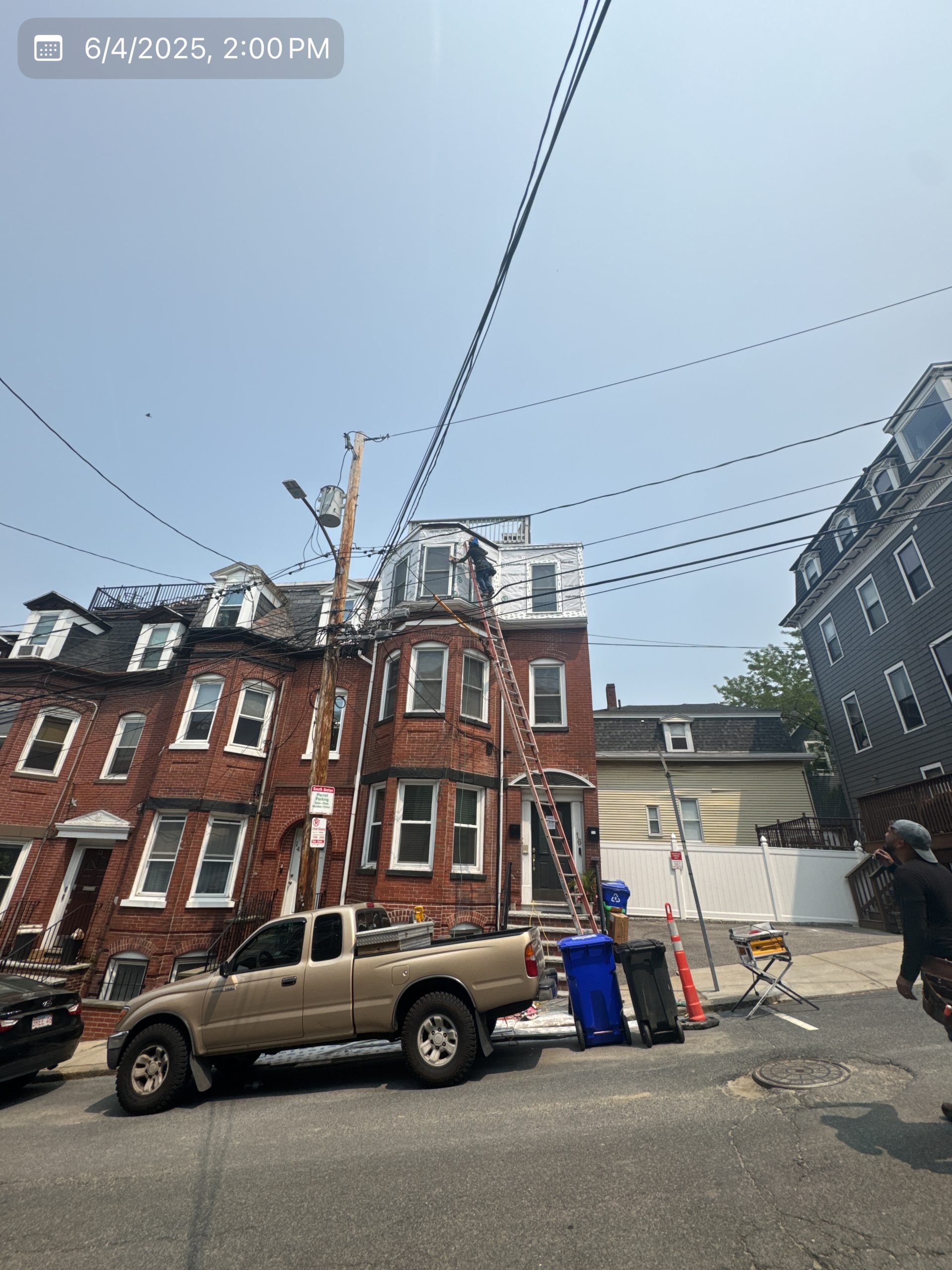 2025-06-04 18 00 21Z-mbi96dq2qxwt9rb0 Street view of a three-story brick apartment building with bay windows and a mansard roof on an overcast day.