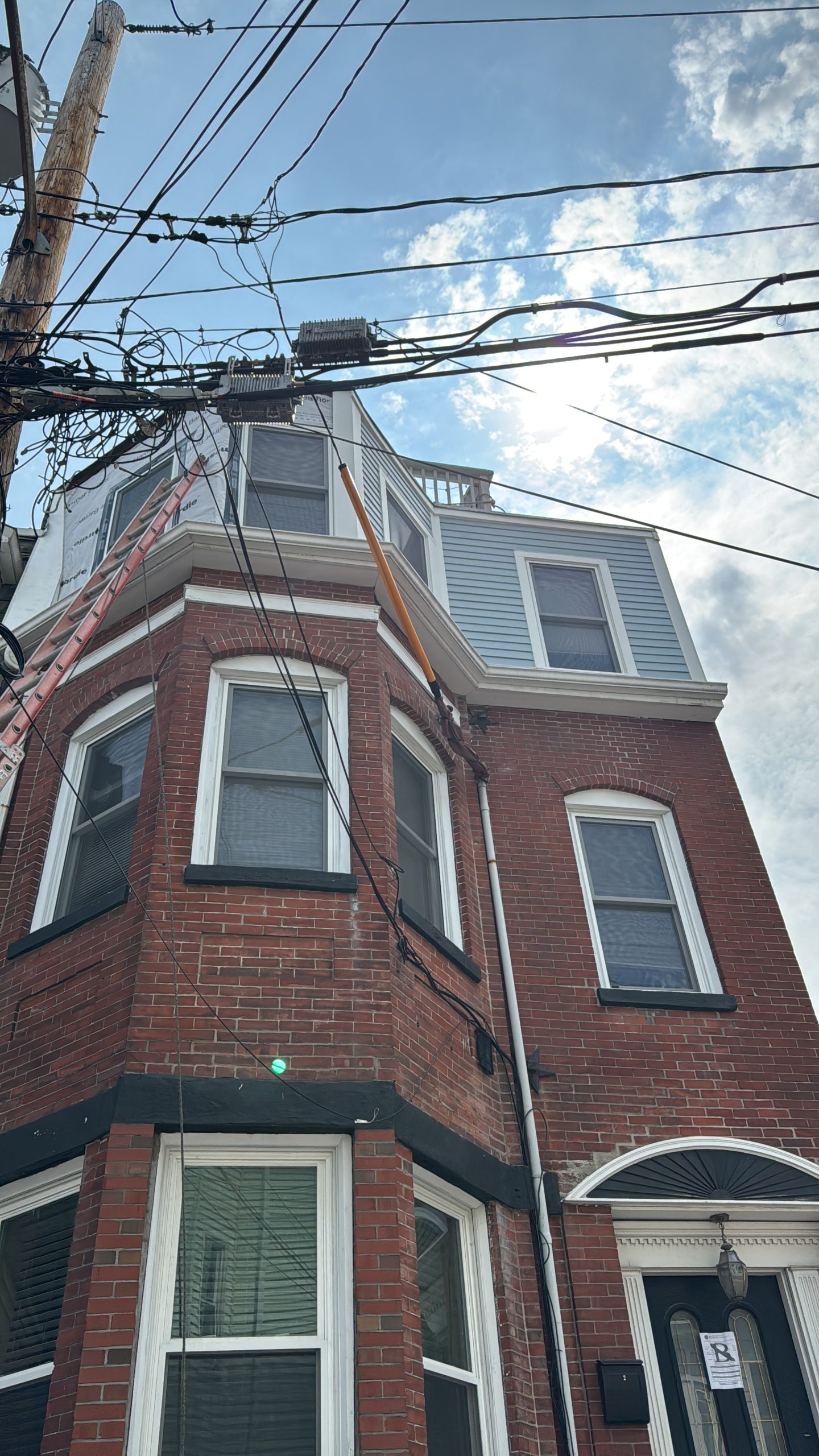 2025-06-09 18 00 10Z-mbpeden1qyul2uyv Street view of a three-story brick apartment building with bay windows and a mansard roof on an overcast day.