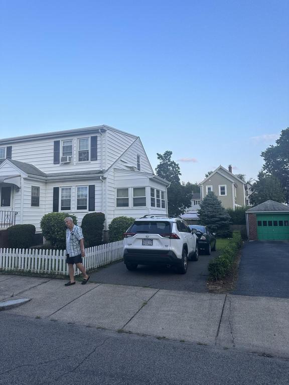 7 24 2023 9 10 20 PM-lkhlo86kek1wobm1 White house with black shutters, a white picket fence, and a person walking on the sidewalk.