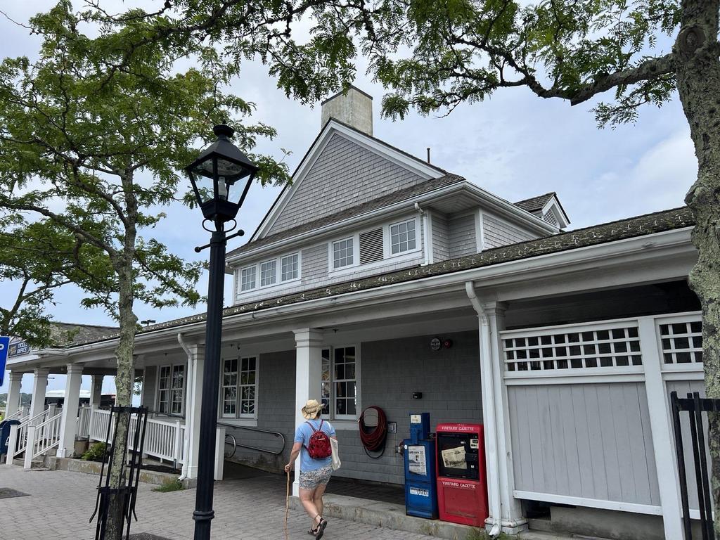 7 28 2023 16 51 19-lkn26jqqfyphfvrs Gray shingle building with a covered porch and a woman walking past.