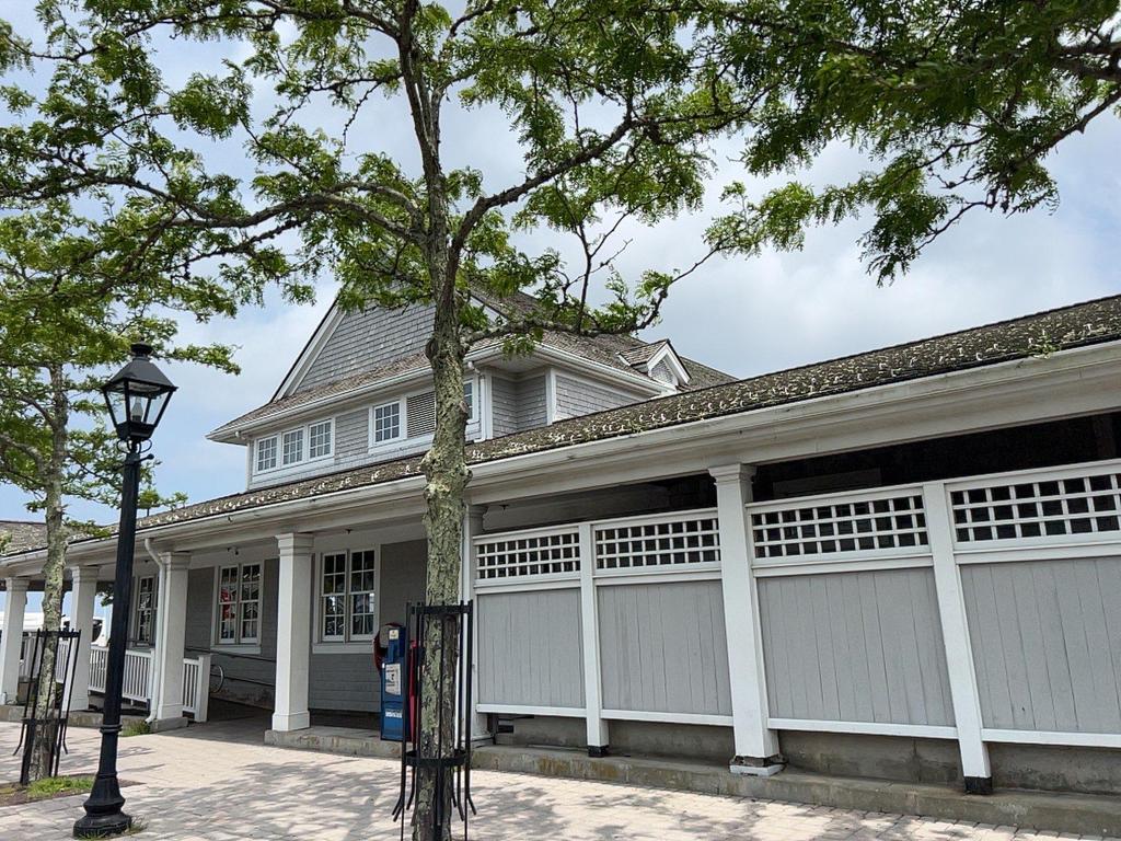 7 28 2023 16 51 19-lkn26jr2i8wezdn3 Gray building with lattice work and large trees in front.
