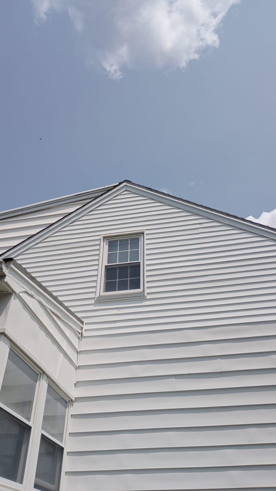 8 3 2023 1 18 15 PM-lkvf7ndksxu7rmo6 Gable end of a white sided house with a single window against a blue sky.