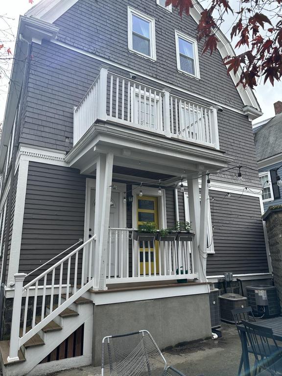 8 3 2023 10 29 20 PM-lkvywcdw4xcwh5m1 Rear exterior of a house with dark brown siding, a small deck with white railings, stairs, and a bright yellow door with planter boxes.