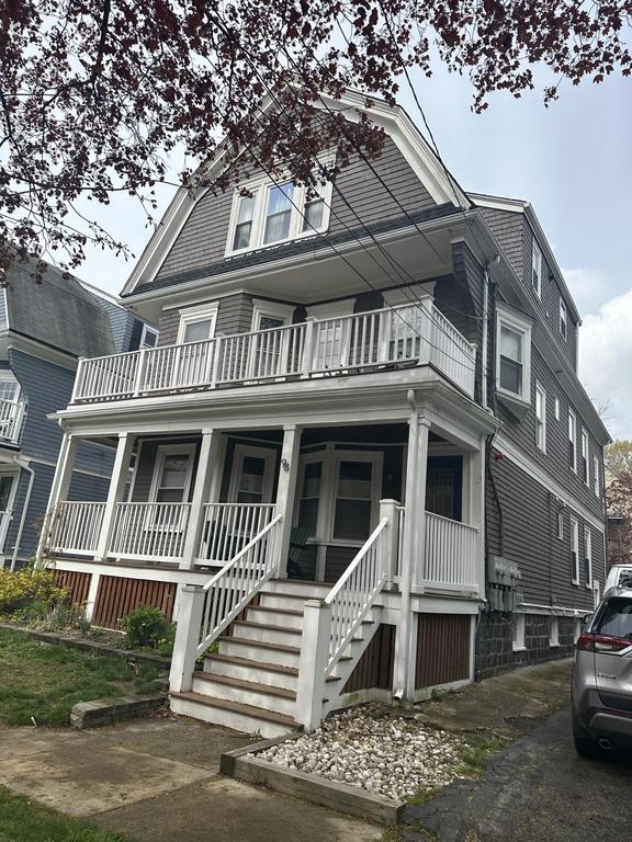 8 3 2023 10 29 20 PM-lkvywce9biyshq7e Three-story house with dark brown siding, a large front porch and second-story balcony with white railings, and mature trees in the foreground.