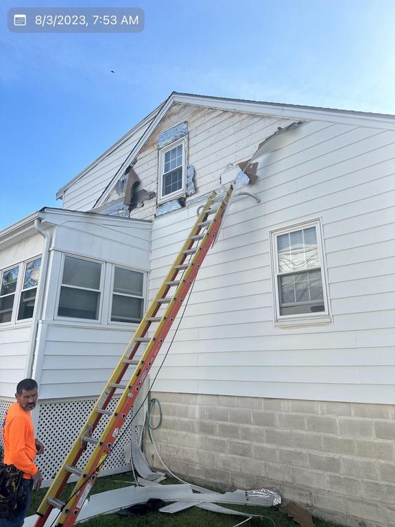 8 3 2023 7 53 09 AM-lkv3lk9ox1wbrtem Contractor on a ladder next to a house with damaged white siding.