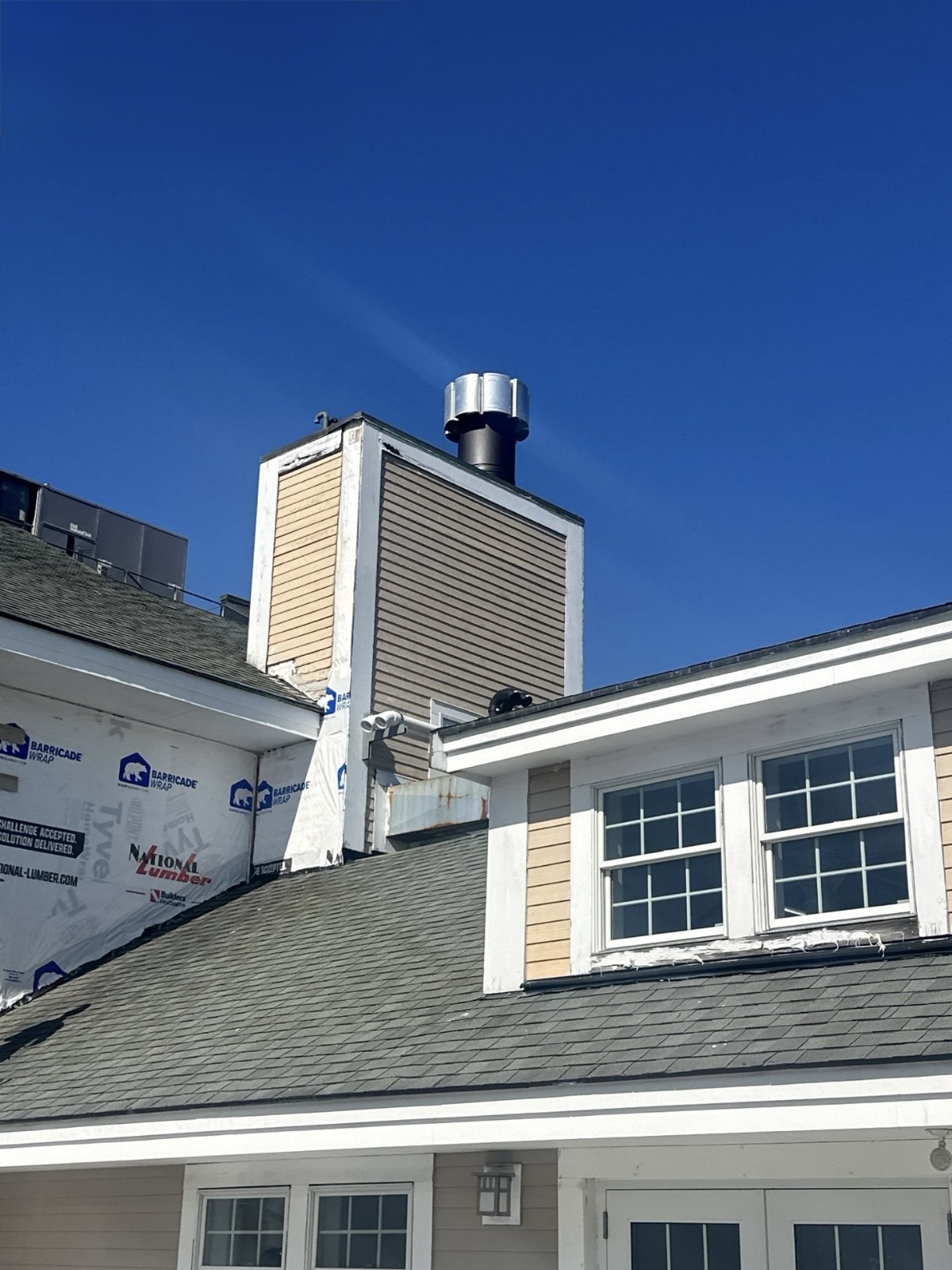 IMG_3693 Rooftop view of a building renovation against a bright blue sky, highlighting the new chimney structure.