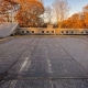 Flat commercial EPDM rubber roof with yellow gas piping and autumn trees in the background.